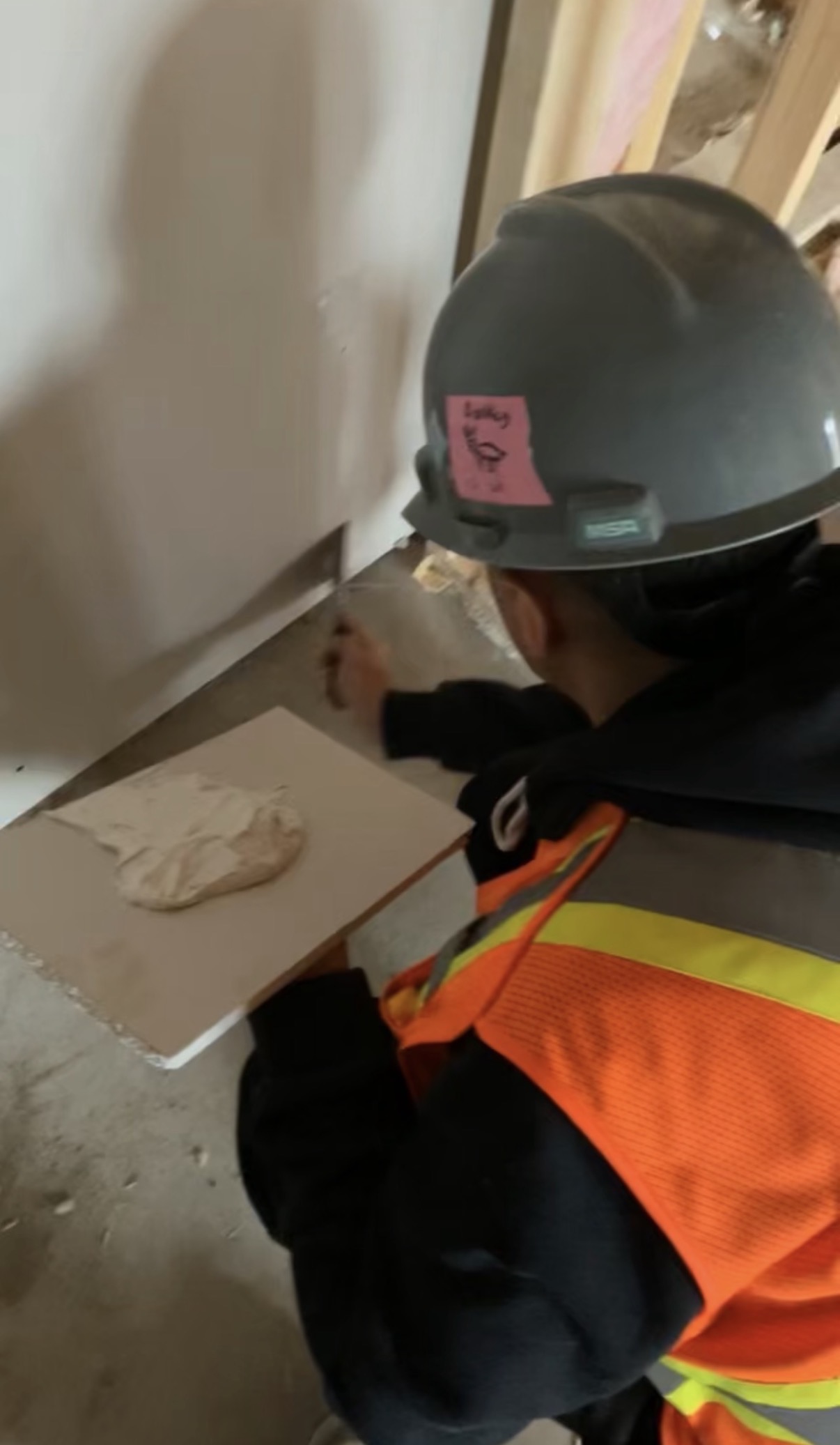 Worker in hard hat and high visibility vest doing finishing work on drywall.